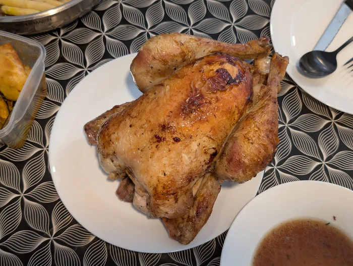 Medio pollo asado, con la piel dorada, en un plato blanco junto a un cuenco con su jugo
